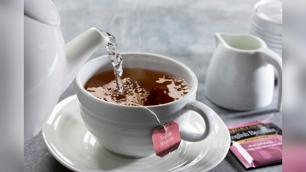 Hot English Breakfast tea being poured into a white cup from a teapot.