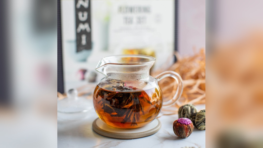 Glass teapot with blooming flower tea, Numi tea box, and floral tea balls