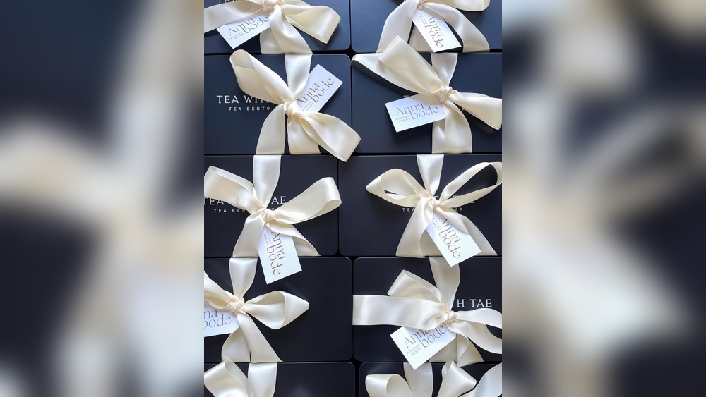 Elegant black gift boxes with cream ribbon bows, some with "Anna Bode" tags.