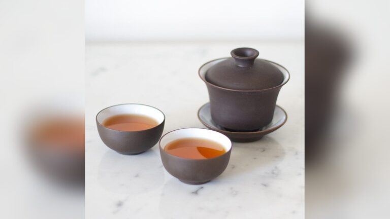 Brown ceramic gaiwan tea set with two cups filled with amber tea.