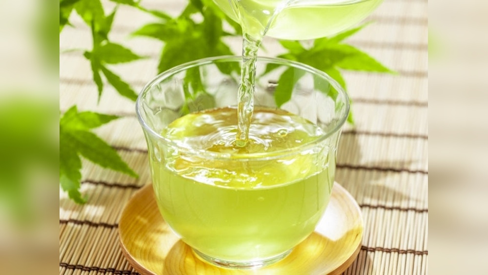 Pouring Gyokuro green tea into a clear glass, showcasing its vibrant green hue.