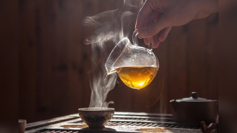Pouring hot tea from a glass teapot into a cup for the best cup of tea.