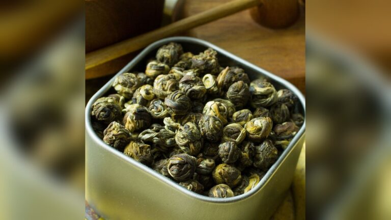 Close-up of dried jasmine tea pearls in a tin, showcasing their intricate rolled shape.