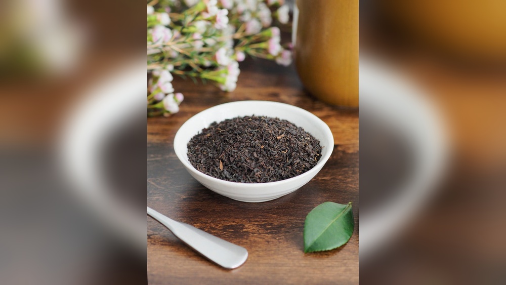 Bowl of loose leaf black tea with a spoon and tea leaf