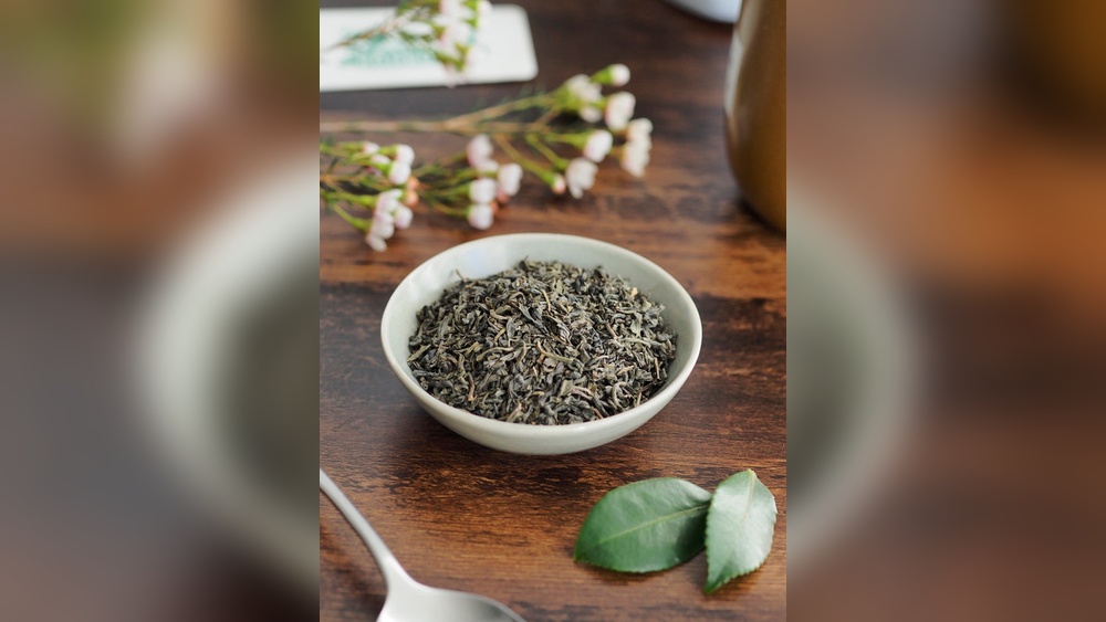 Bowl of loose leaf green tea with fresh leaves and delicate white flowers