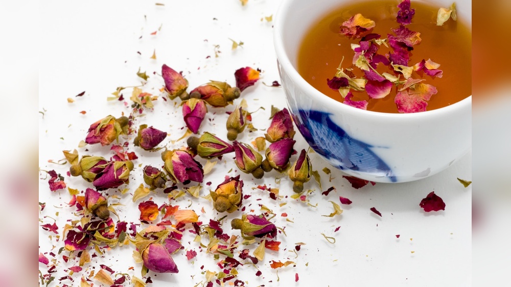 Rose bud tea in a cup with scattered dried rose buds and petals