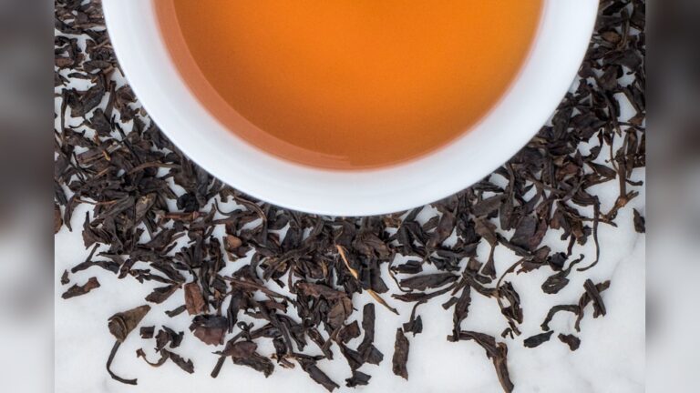 Bowl of amber Lapsang Souchong tea surrounded by dark, smoky tea leaves