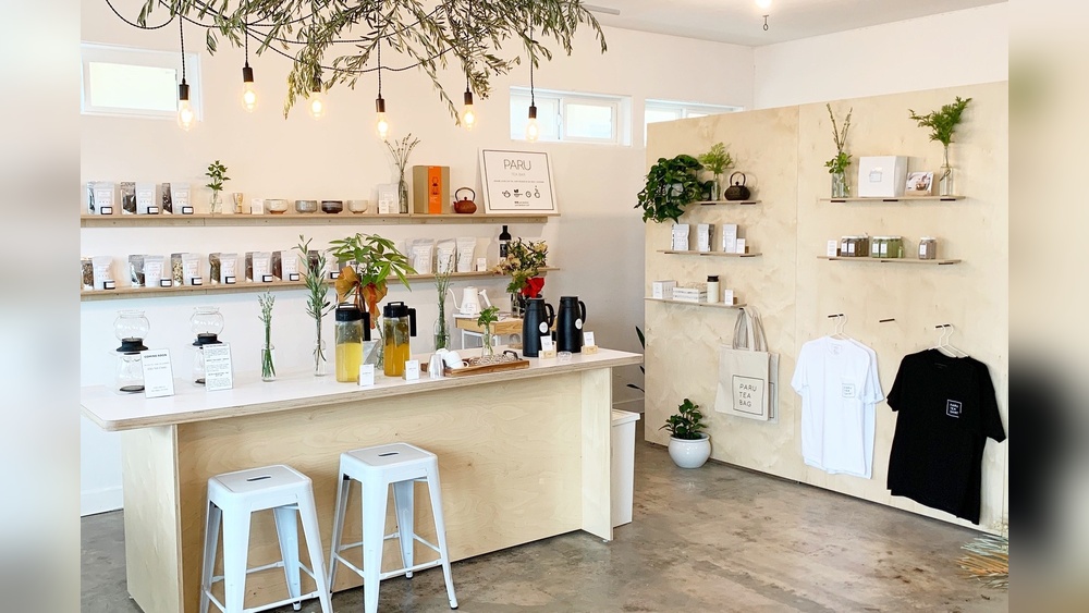 Interior of a specialty tea shop with shelves of tea, a counter with stools, and hanging plants.