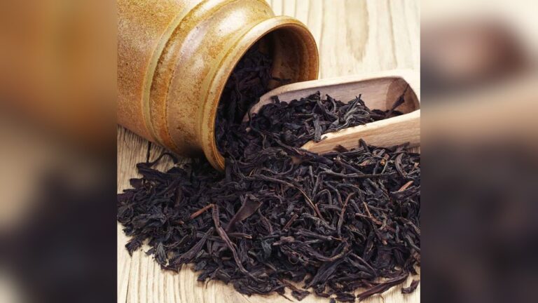 Loose black tea leaves spilling from a ceramic pot onto a wooden surface.