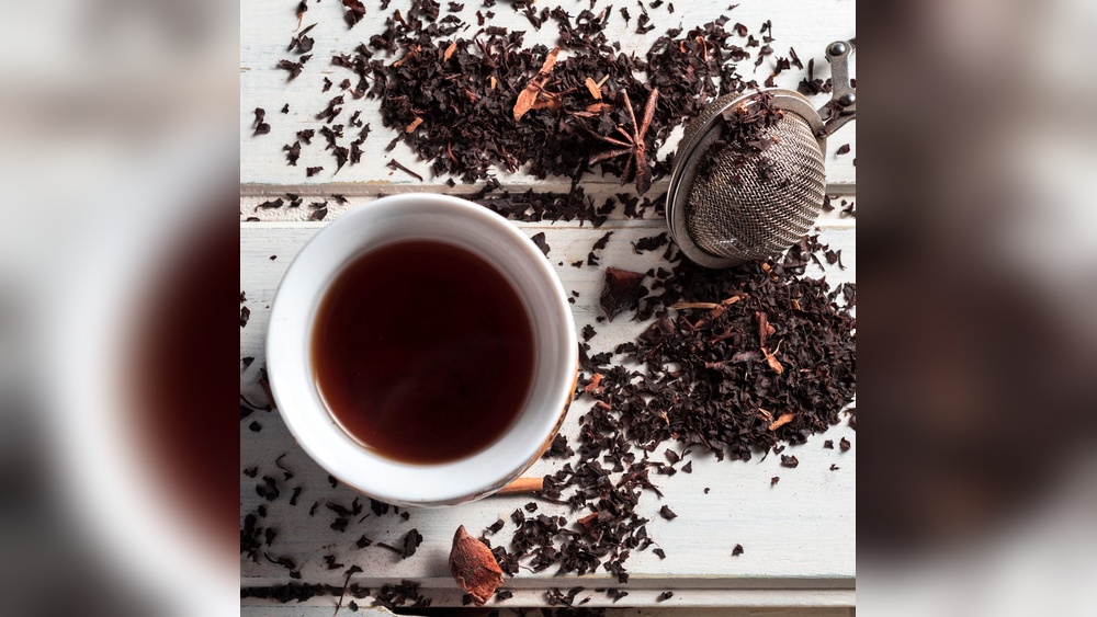 Loose black tea leaves and a cup of brewed black tea, with a tea strainer.