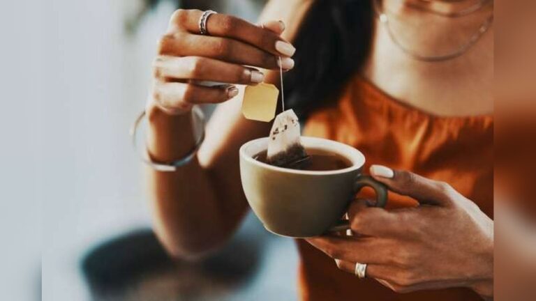 Woman steeping black tea bag in a cup, relevant to daily intake.