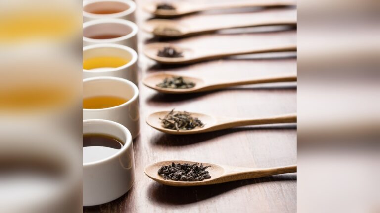 Wooden spoons with tea leaves next to cups of tea