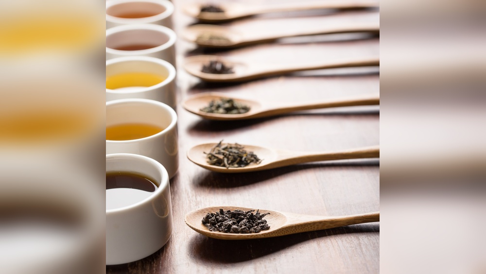 Wooden spoons with tea leaves next to cups of tea